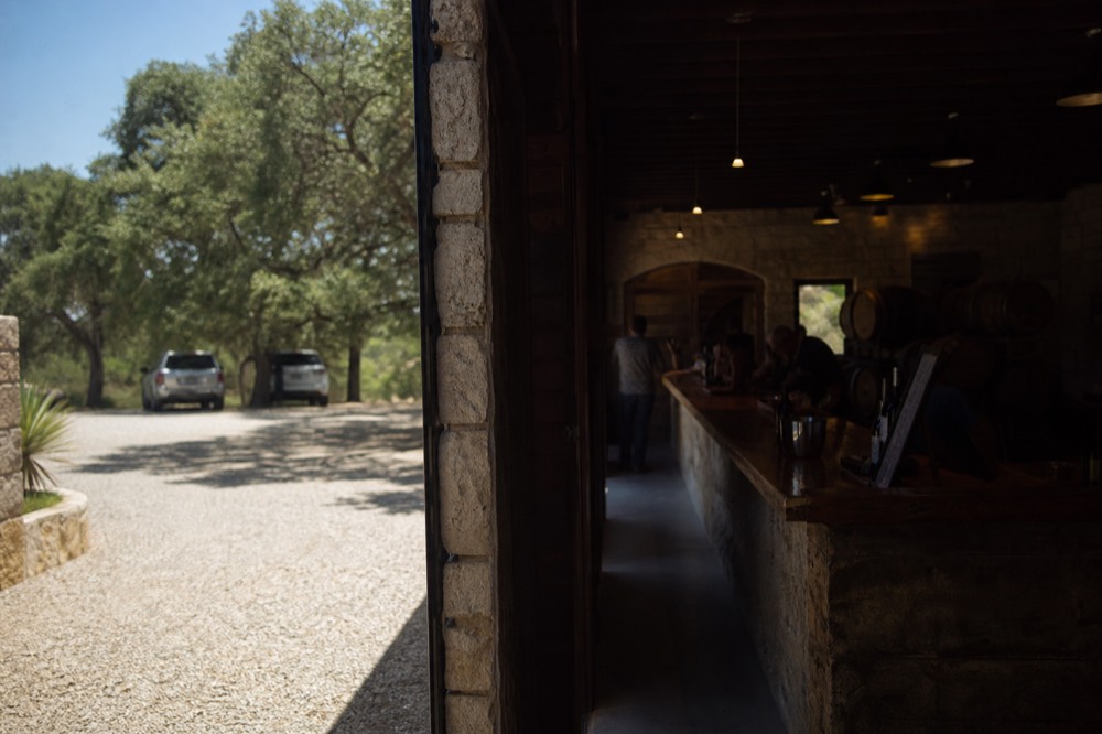 Cool dim interior of a stone tasting room with a long wooden bar, stacked barrels and soft overhead lighting
