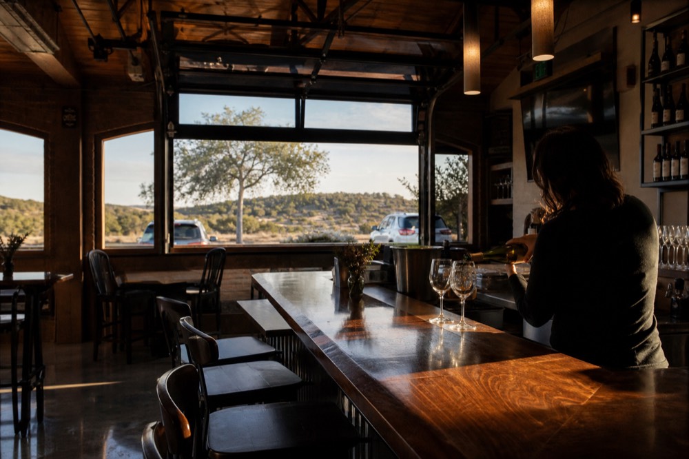Nearly empty winery tasting bar on a weekday morning with sunlight across polished wood and a single staff member pouring