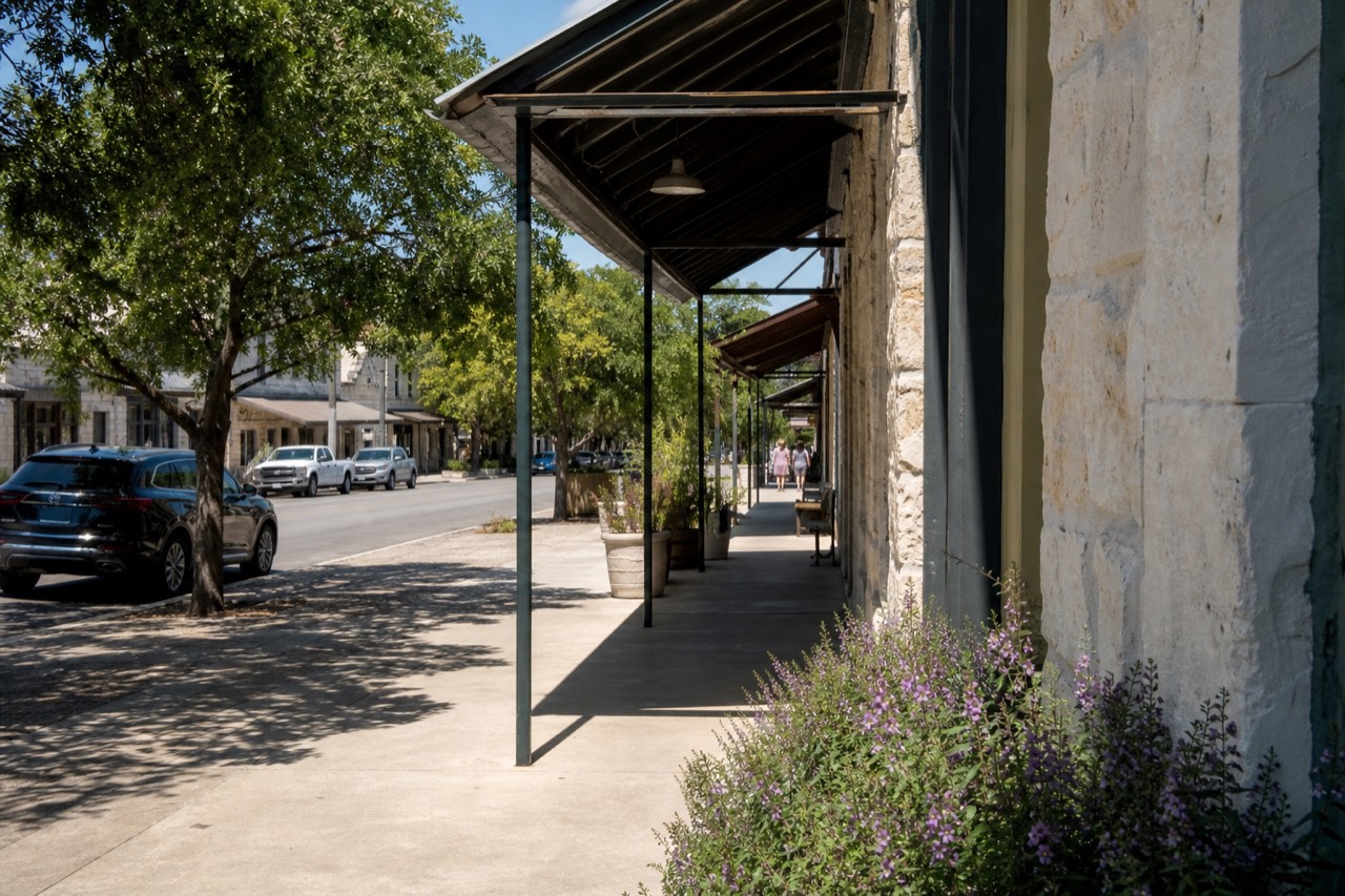Wide sidewalk along a historic Texas Main Street with limestone storefronts and awnings on a bright afternoon