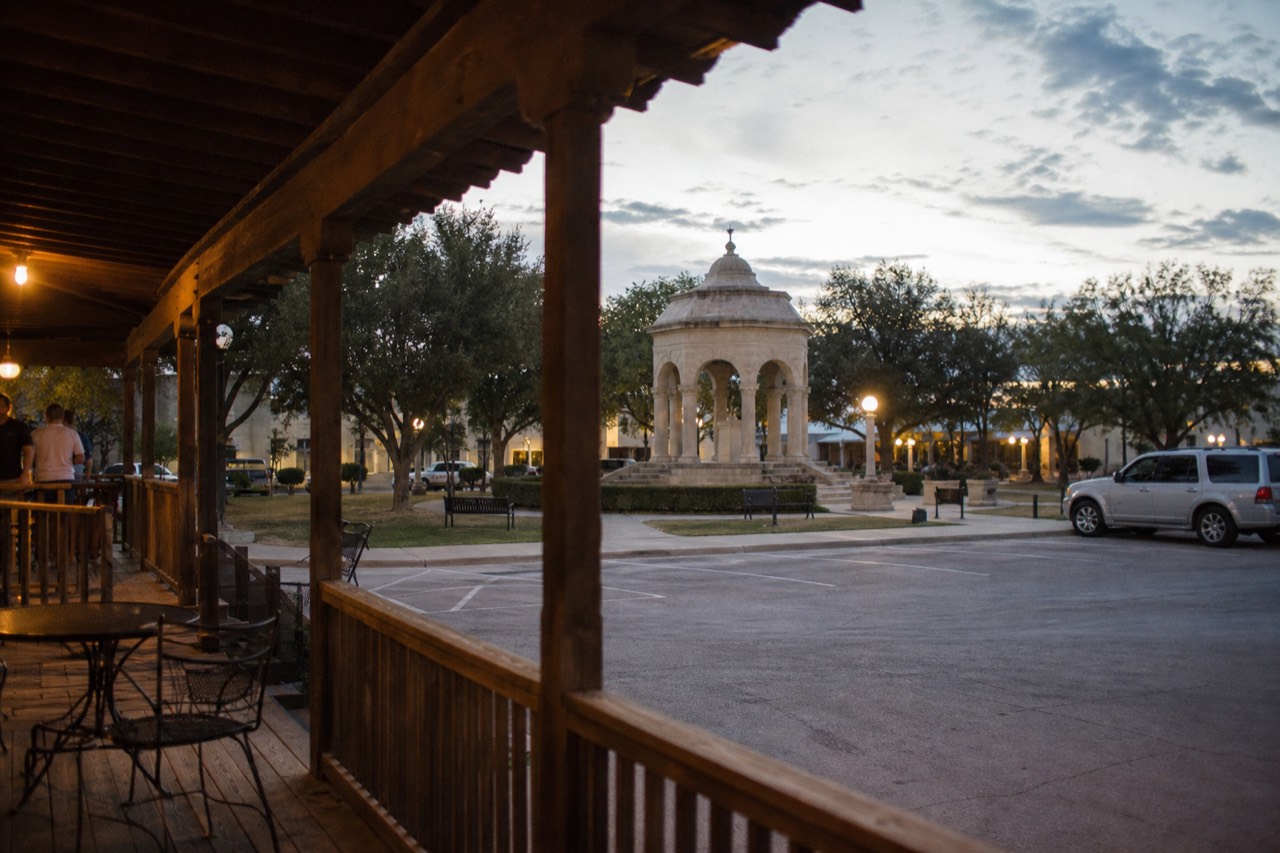 A quiet German-Texan town square with an eight-sided stone landmark, shade trees and empty benches in early morning light