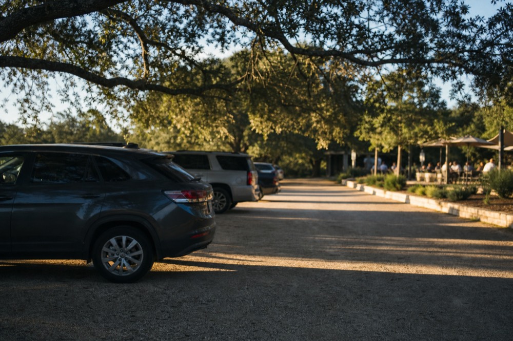 A gravel and decomposed granite winery car park with a low limestone kerb separating it from a shaded tasting patio