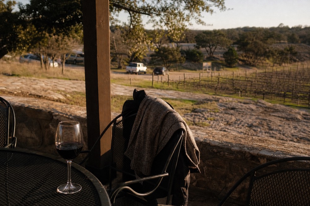 A wool jumper and waterproof shell draped over the back of a chair beside a glass of red wine on a winter patio table