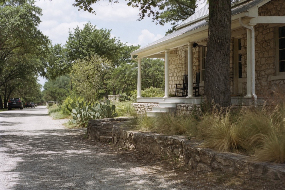 A restored stone guesthouse with a wide porch and rocking chairs on a quiet residential street in a Texas hill town