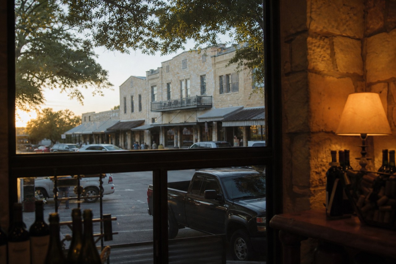 Historic limestone storefronts along a small Texas main street at golden hour with shade trees and parked cars