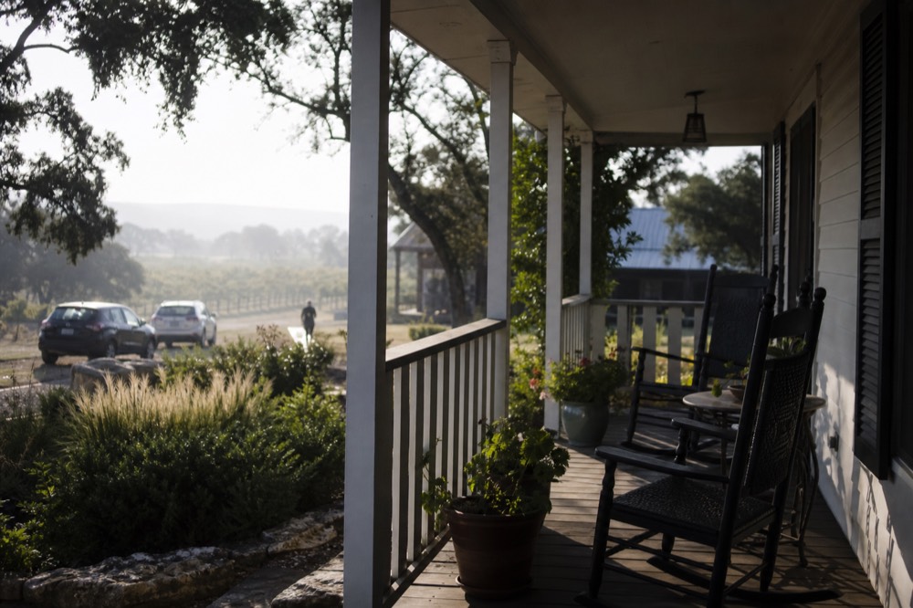 A deep shaded porch on a white clapboard guesthouse with two rocking chairs, a small side table and potted plants along the rail