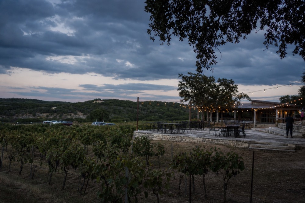 Dark storm clouds gathering over a Texas vineyard with rows of vines in the foreground and empty outdoor tables